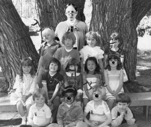An elementary school class photo shows four children with antlers and deer noses. The teacher standing behind them looks very severe.