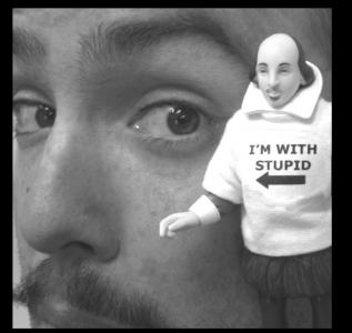 A black-and-white close-up of a man's face. In front of him is a small William Shakespeare figurine wearing a shirt that says “I’m with stupid” and an arrow pointing to the man's face.