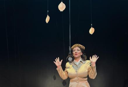 A 1940's woman is standing an old fashioned looking microphone that is hanging from the ceiling. She is holding both her hands up in exclamation about how wonderful an onion sandwich can be. Above her, hanging, as if suspended mid air, are three similar painted 2- demensional onions.
